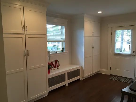 White cabinets and bench in a room with a window and a door, dark wood floor.