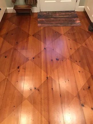 Wooden floor with diamond pattern, near a door and mat.