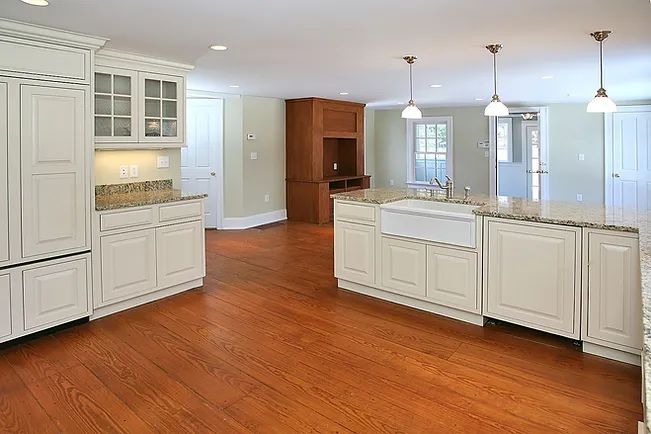 Custom Kitchen Remodeling Spacious kitchen with wood floors, light cabinets, granite countertops, and a farm sink.