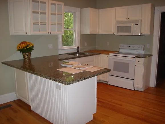 White kitchen with granite countertops, white cabinets, and a hardwood floor.
