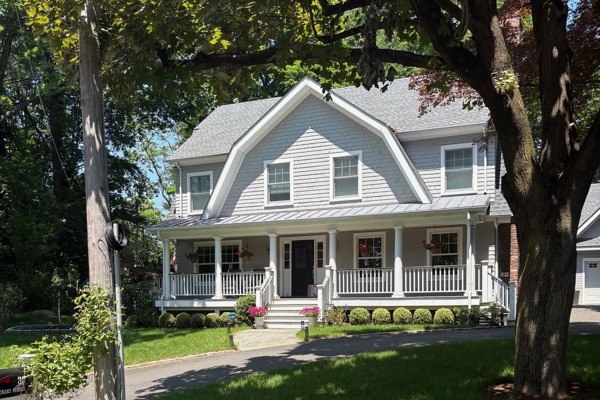 Two-story gray house with a porch and dormer windows, set among green trees and lawn.