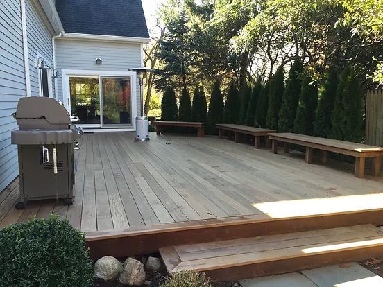 Backyard deck with wooden benches, a grill, and privacy hedges.