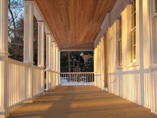 Long covered porch with white columns and railing. Warm light.