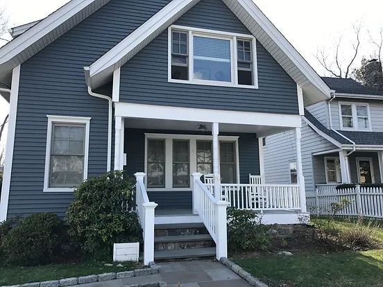 Blue house with white trim, porch, and steps; sunny outdoor setting.