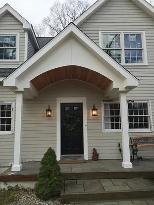 Tan house with white trim, arched doorway, black door, and lantern-style lights.