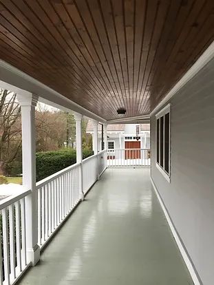 Long porch with a wooden ceiling, white railings, and gray walls.