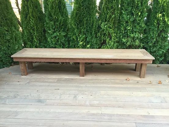 Wooden bench on a light wood deck, with green trees in the background.