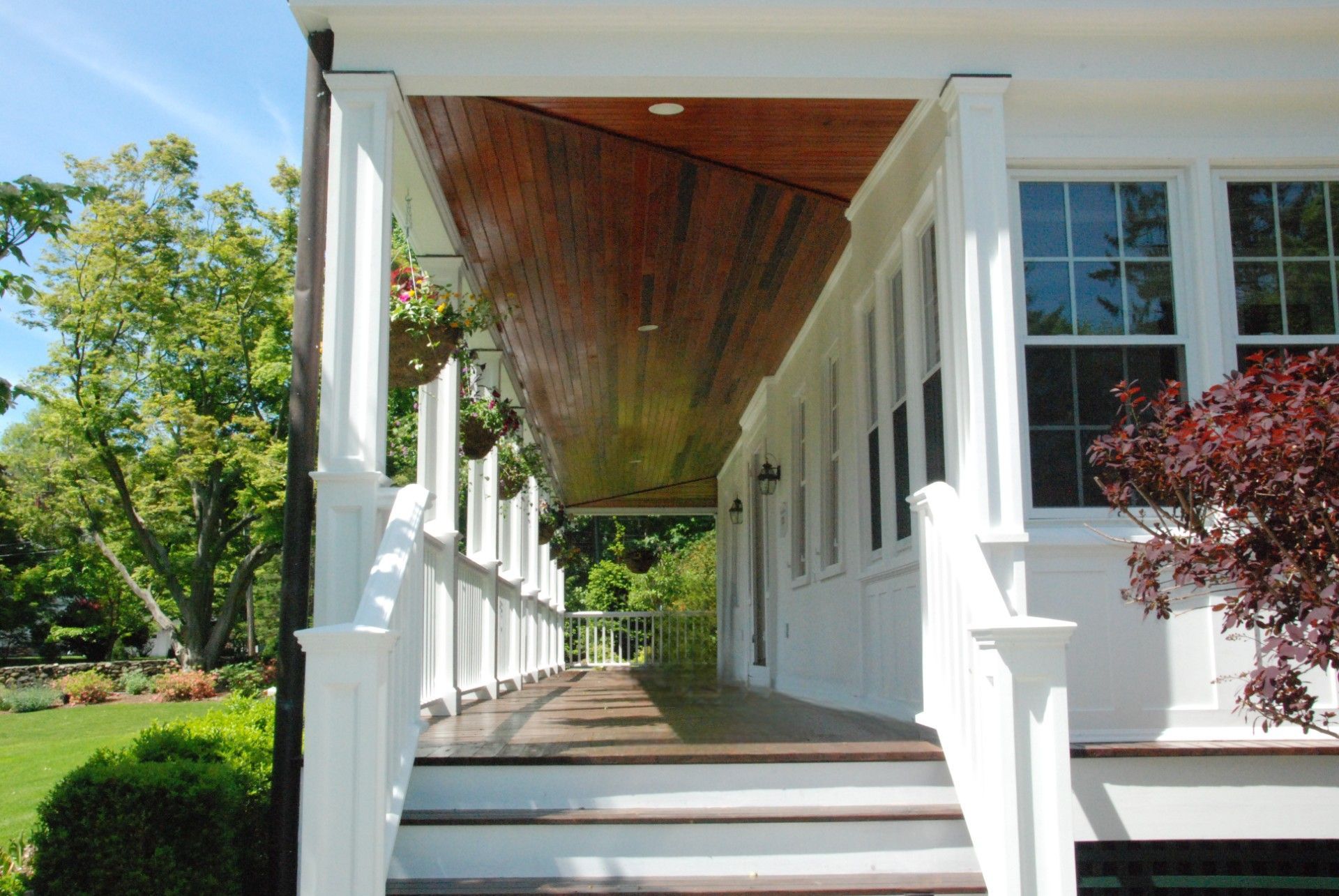 White porch with stairs and columns, brown ceiling, windows, and green yard.