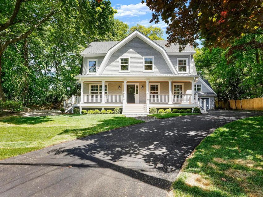 Gray two-story house with front porch, driveway, and lush green lawn under a sunny sky.