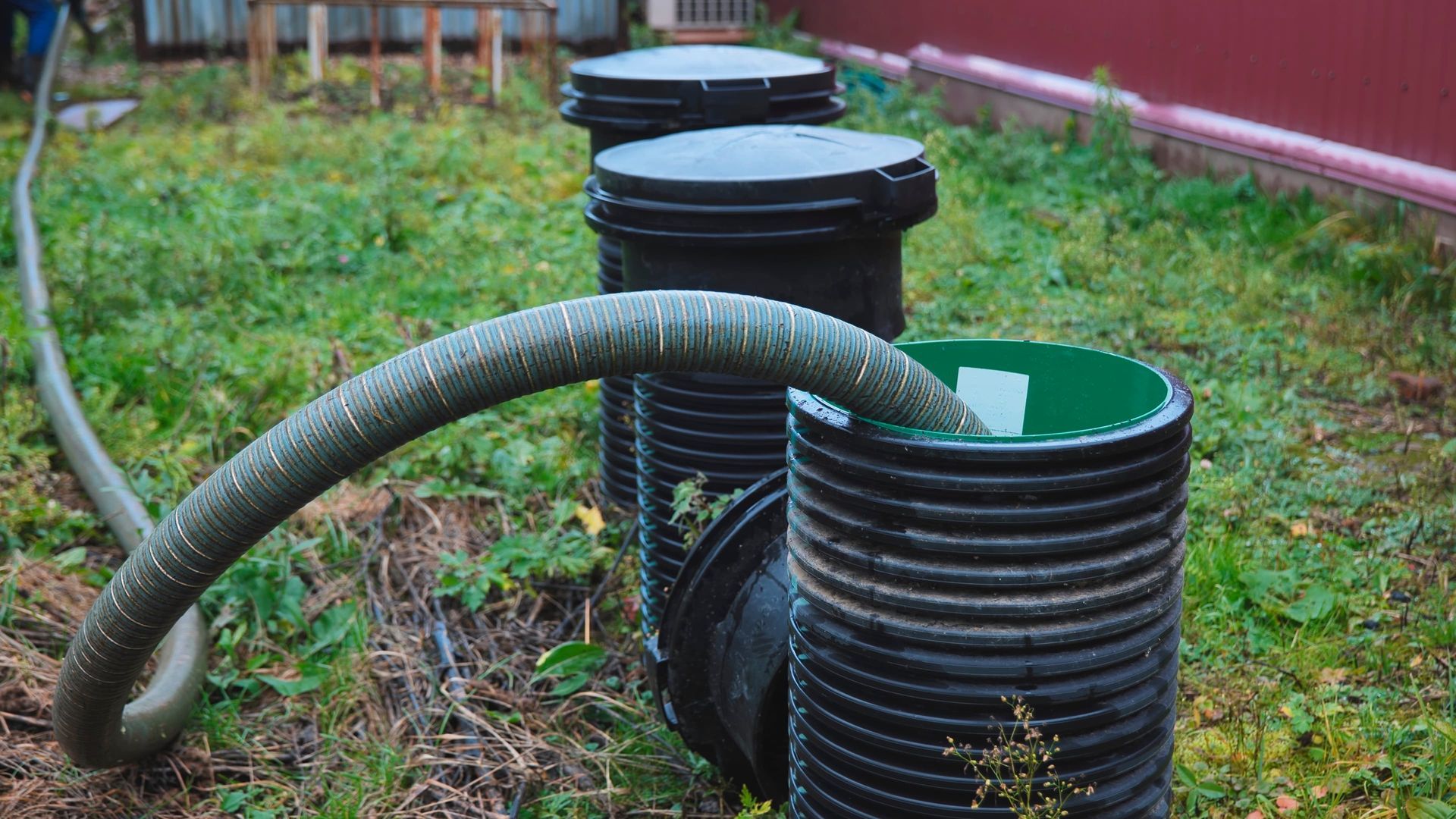 Black corrugated pipes and hose in a grassy garden beside black drainage containers