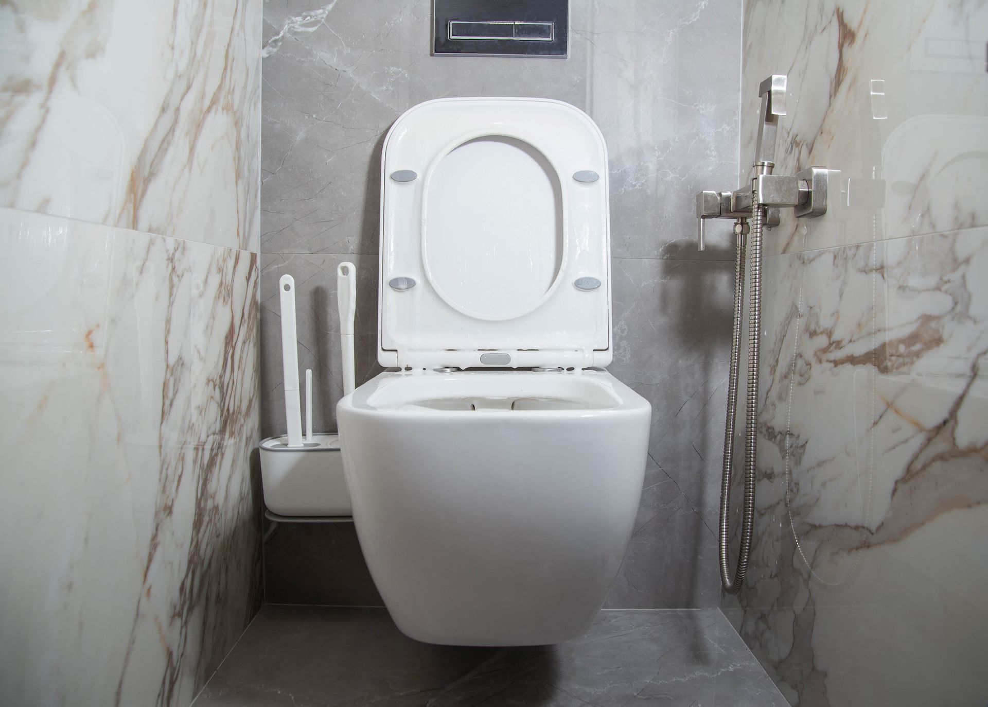 Modern bathroom with a wall-mounted toilet, marble tiles, and handheld bidet spray