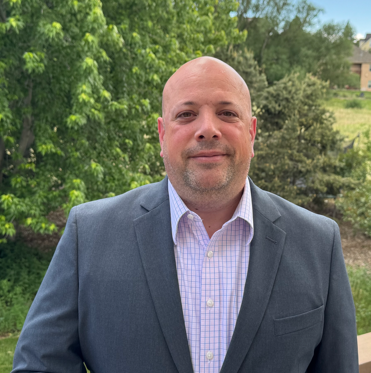 James Anderson A man in a suit and striped shirt is standing in front of trees. James Anderson