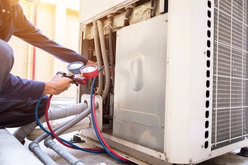 Technician using tools to service an outdoor air conditioner unit with attached hoses