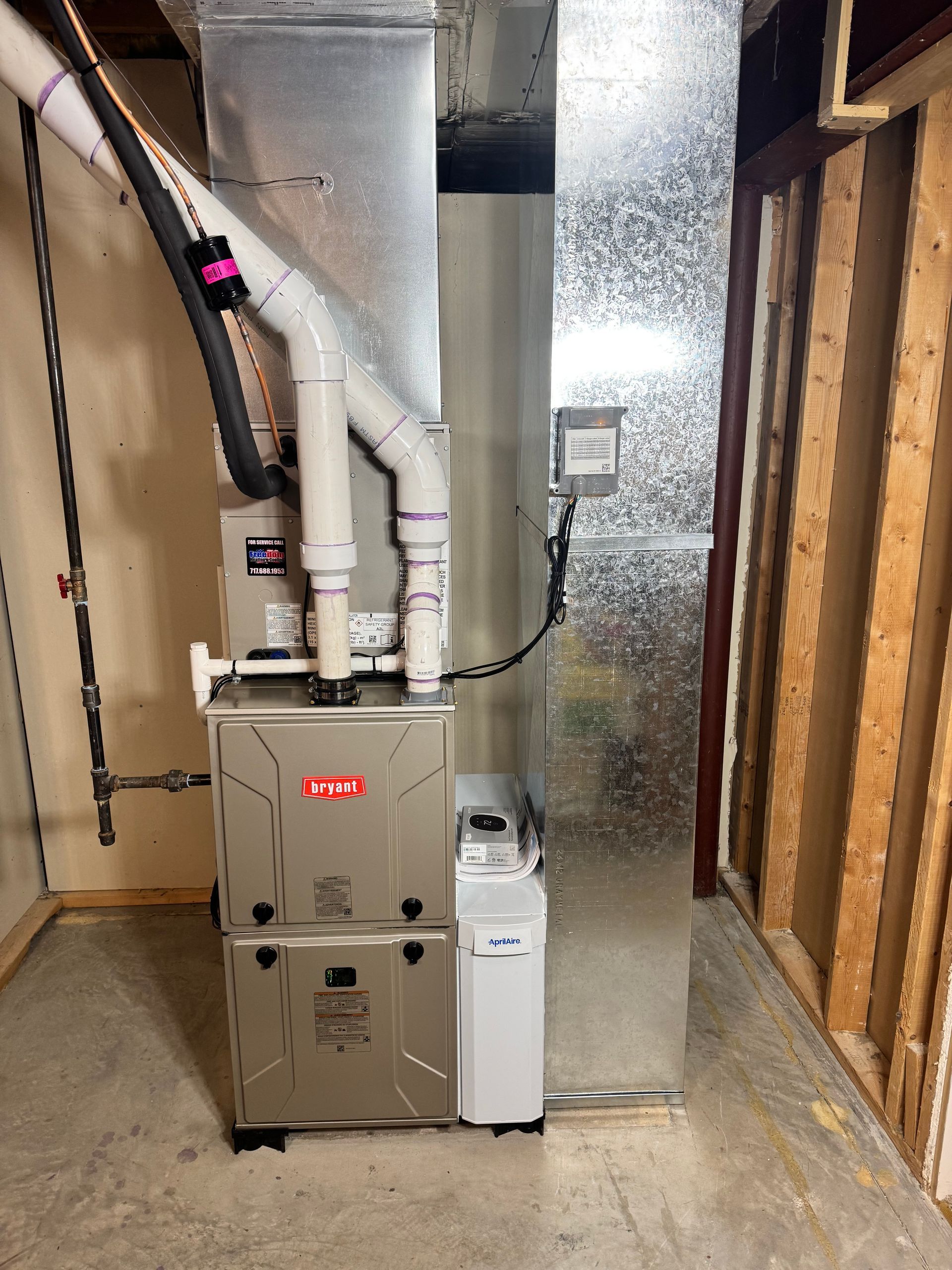 Furnace and water heater in a small utility closet with exposed ducts and reflective insulation panel.