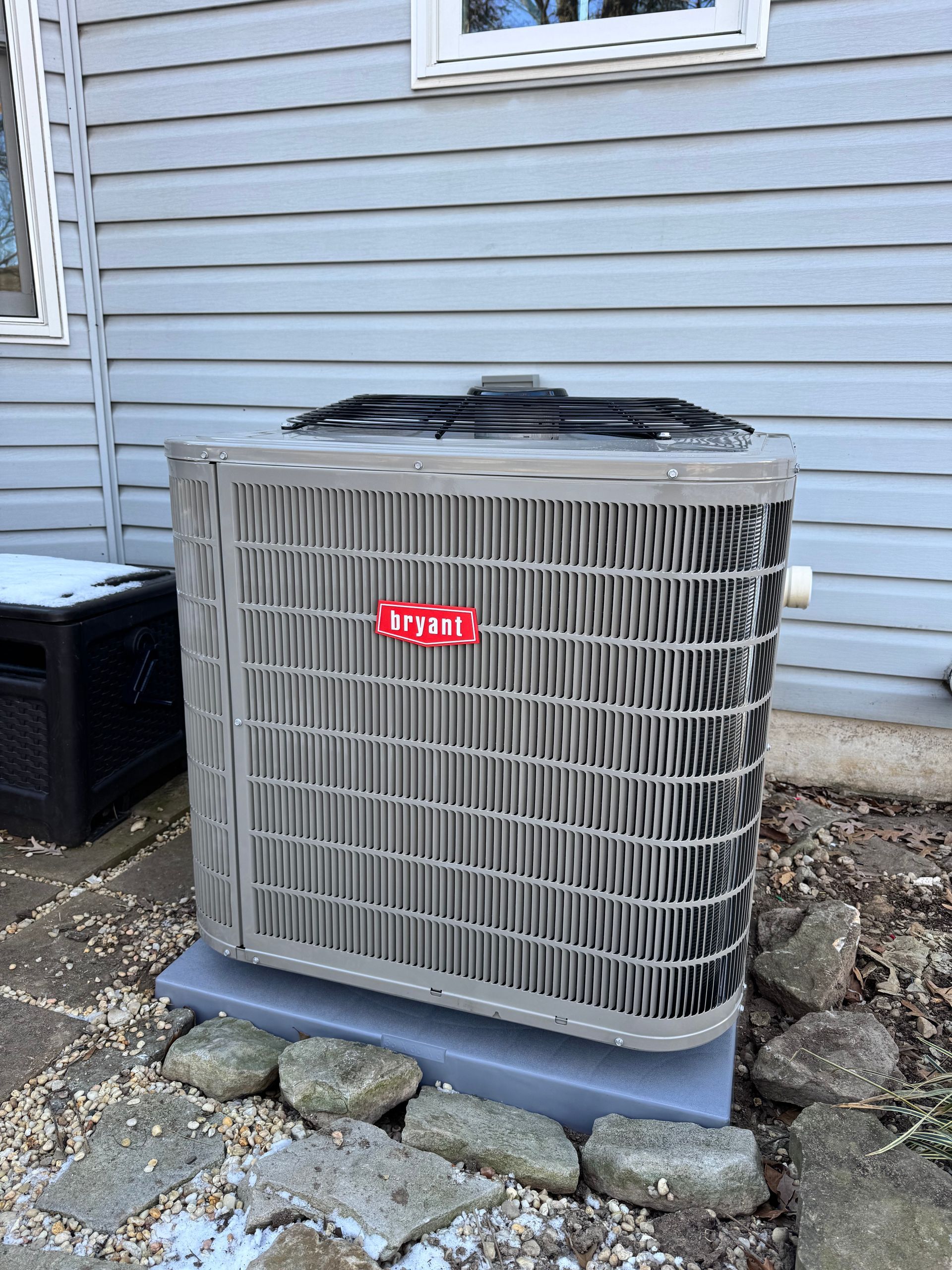 Outdoor air conditioner unit beside a gray house wall and stone path