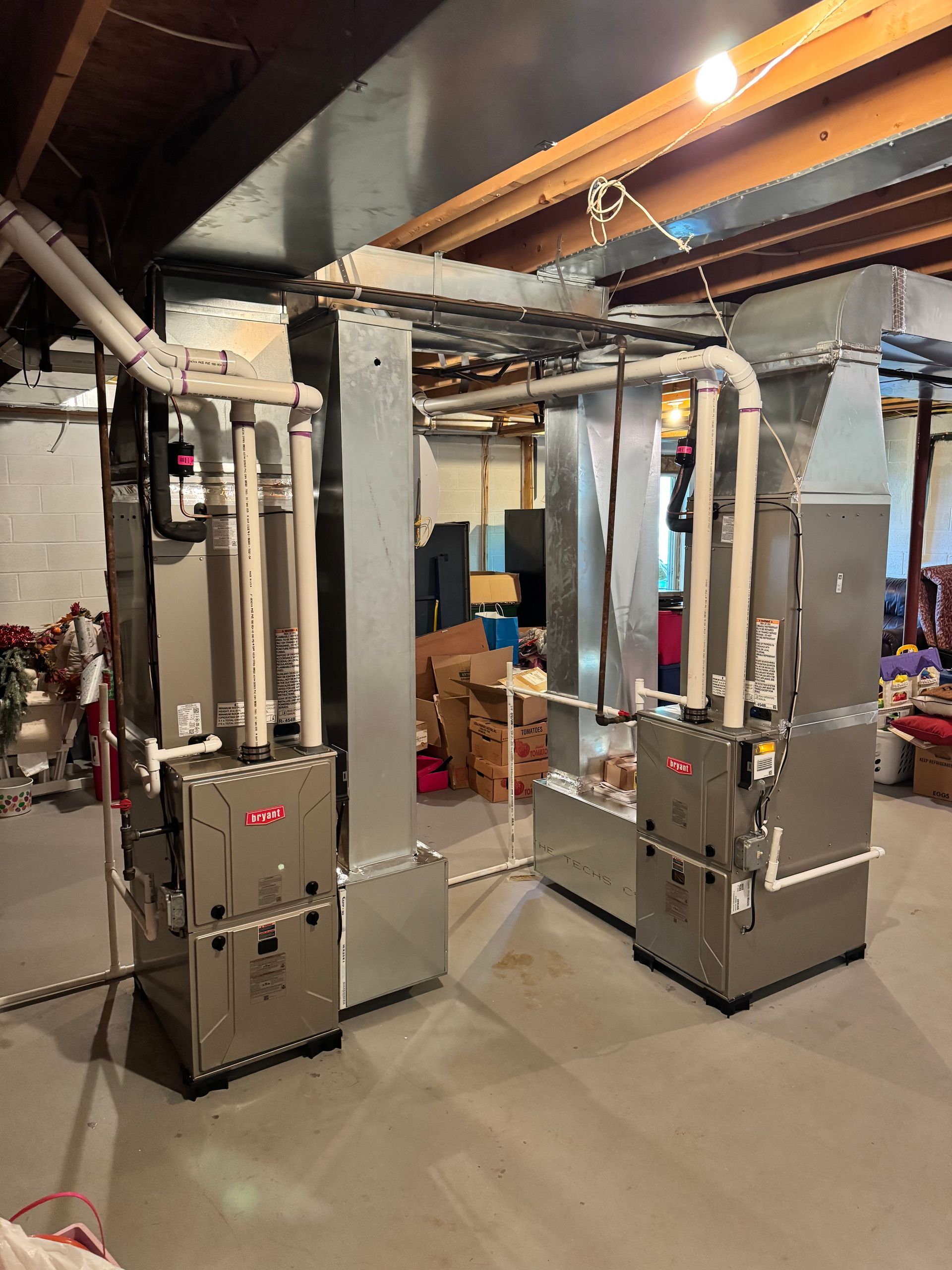 Two tall metal furnaces with ducts and pipes in a basement utility room