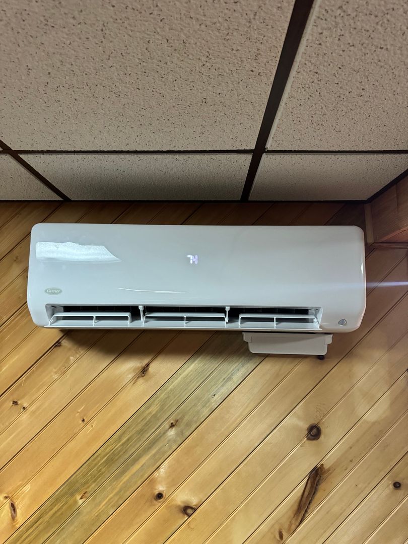 White wall-mounted air conditioner above wood-paneled wall and suspended ceiling tiles