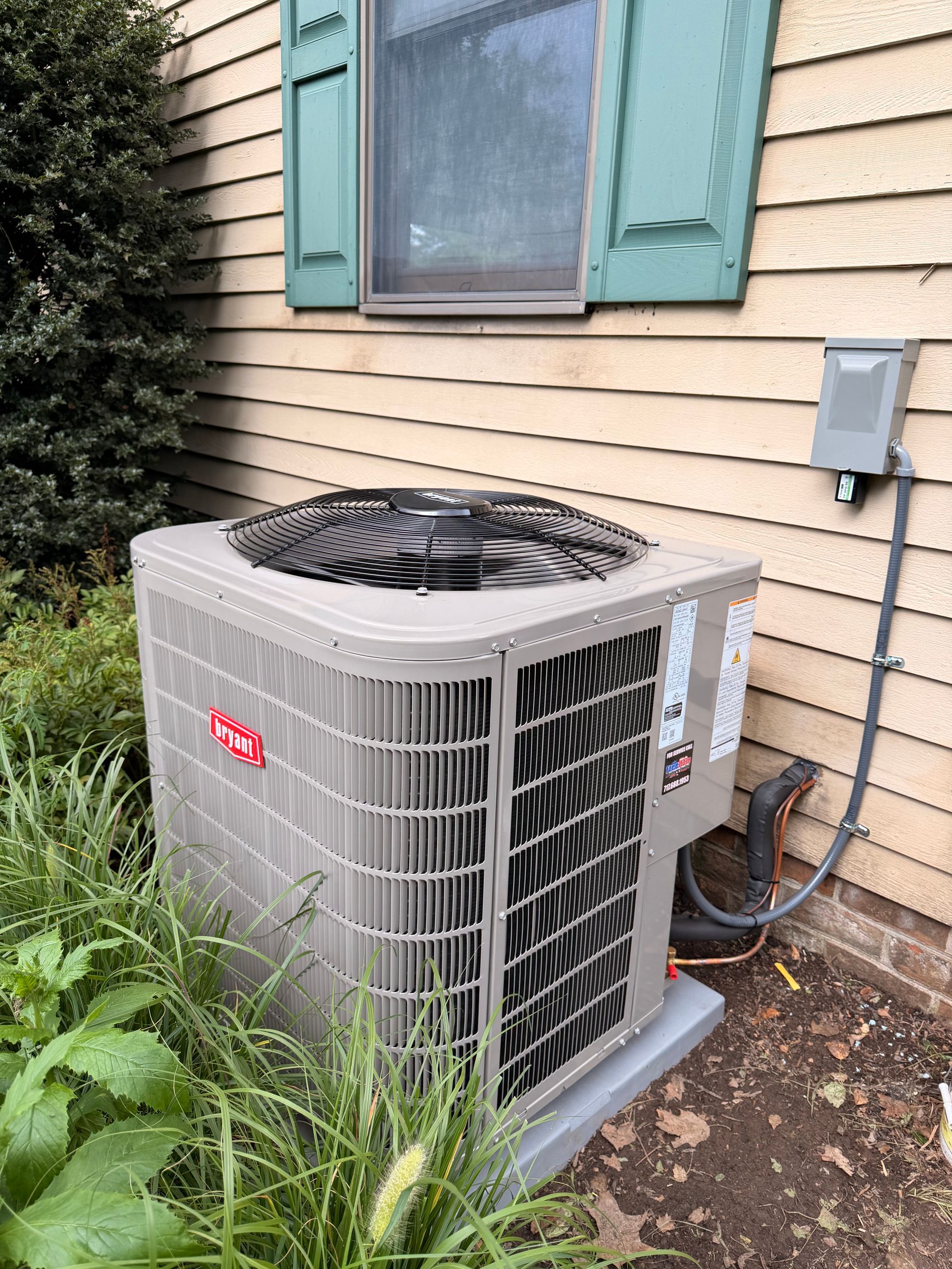 Outdoor air conditioner unit beside a house wall with beige siding and green shutters