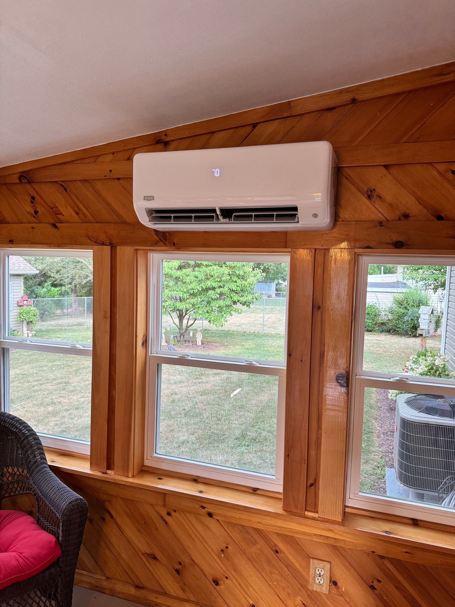 Wall-mounted mini-split AC above windows in a wood-paneled room.