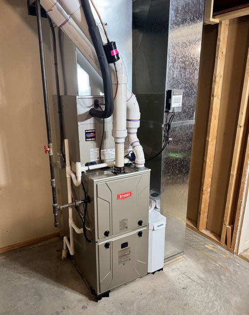 Gray HVAC furnace and white vent pipes installed in a basement utility room near exposed wall framing.