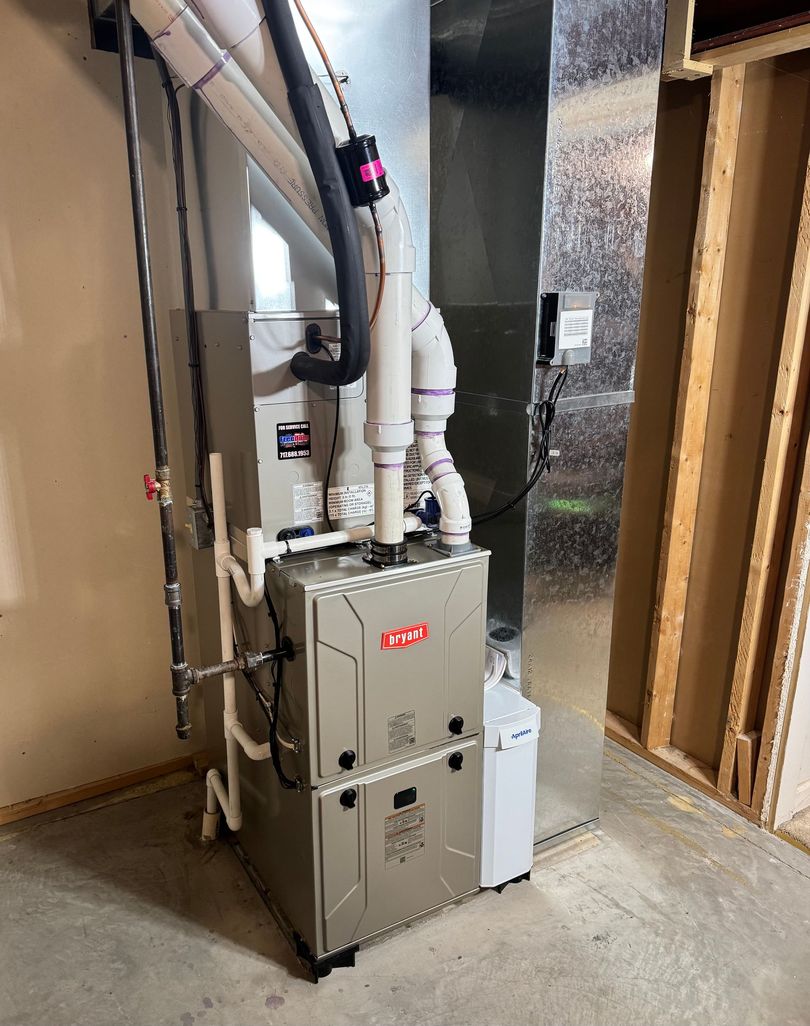 Gray HVAC furnace and white vent pipes installed in a basement utility room near exposed wall framing.