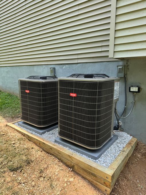 Two outdoor HVAC heat pump units beside a house wall on a gravel pad.