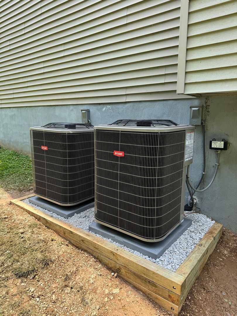 Two outdoor HVAC heat pump units beside a house wall on a gravel pad.