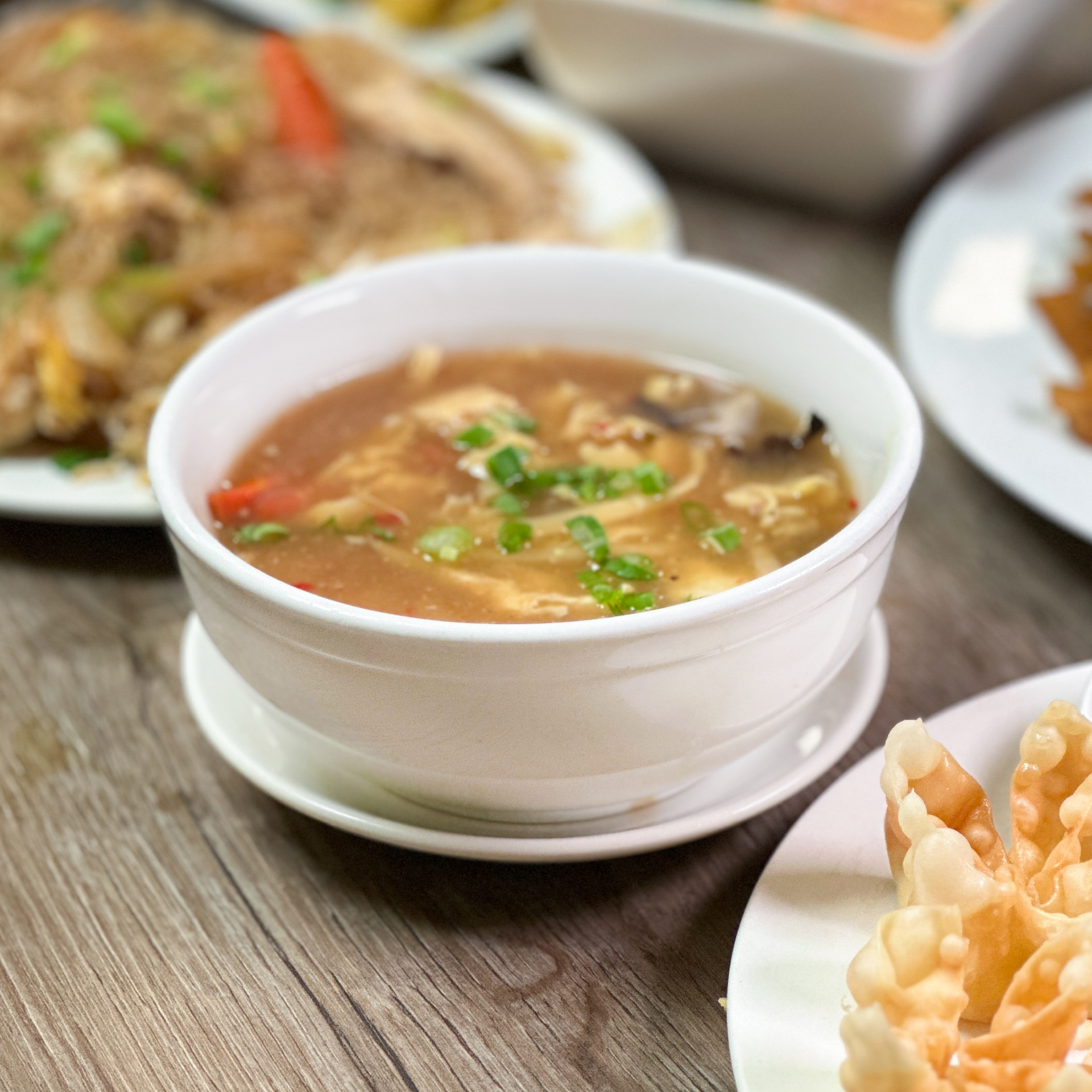 A bowl of soup sits on a table next to plates of food