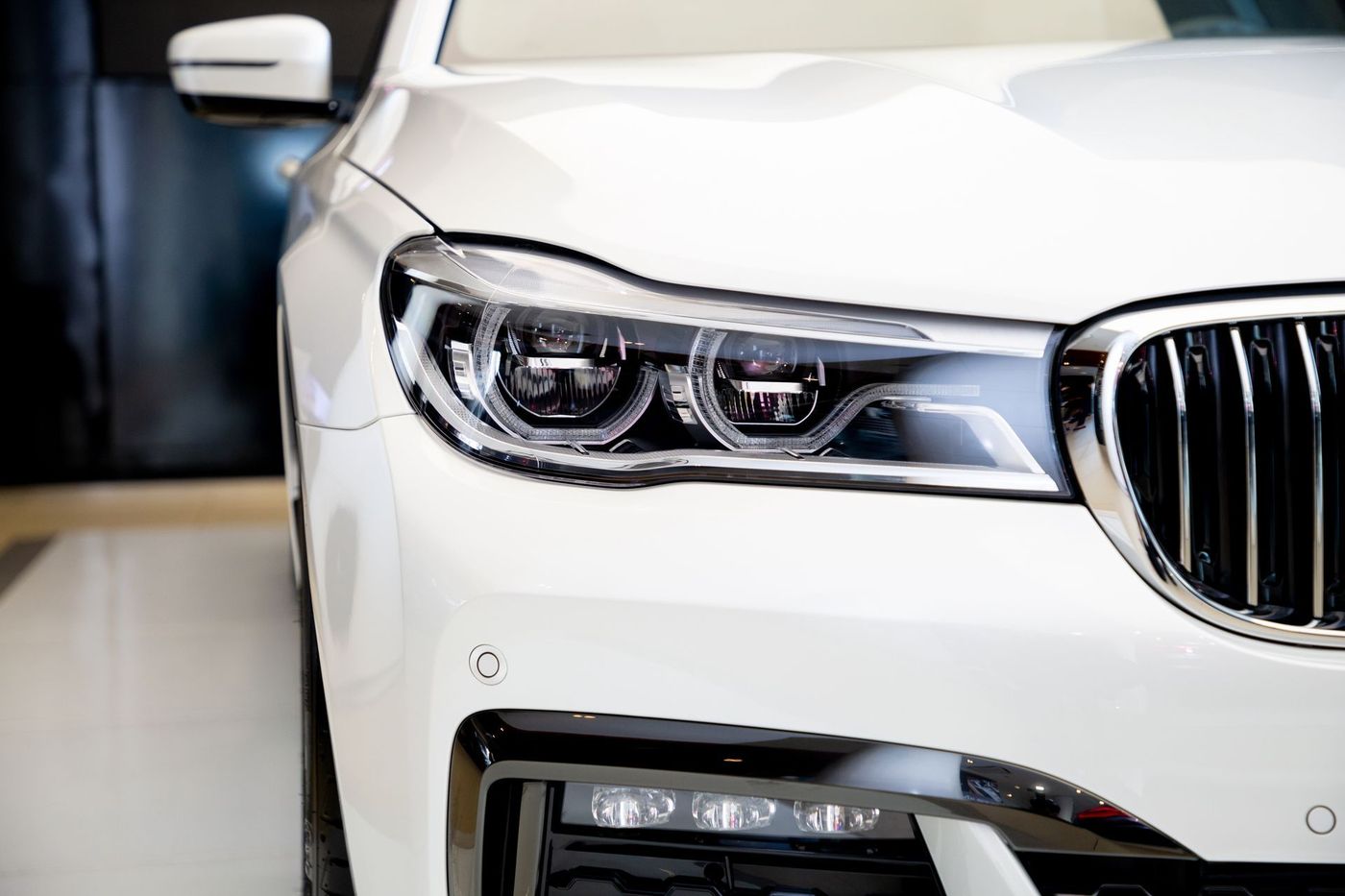 White luxury sedan front end with chrome grille and headlights in an indoor showroom | Walt's Auto Service