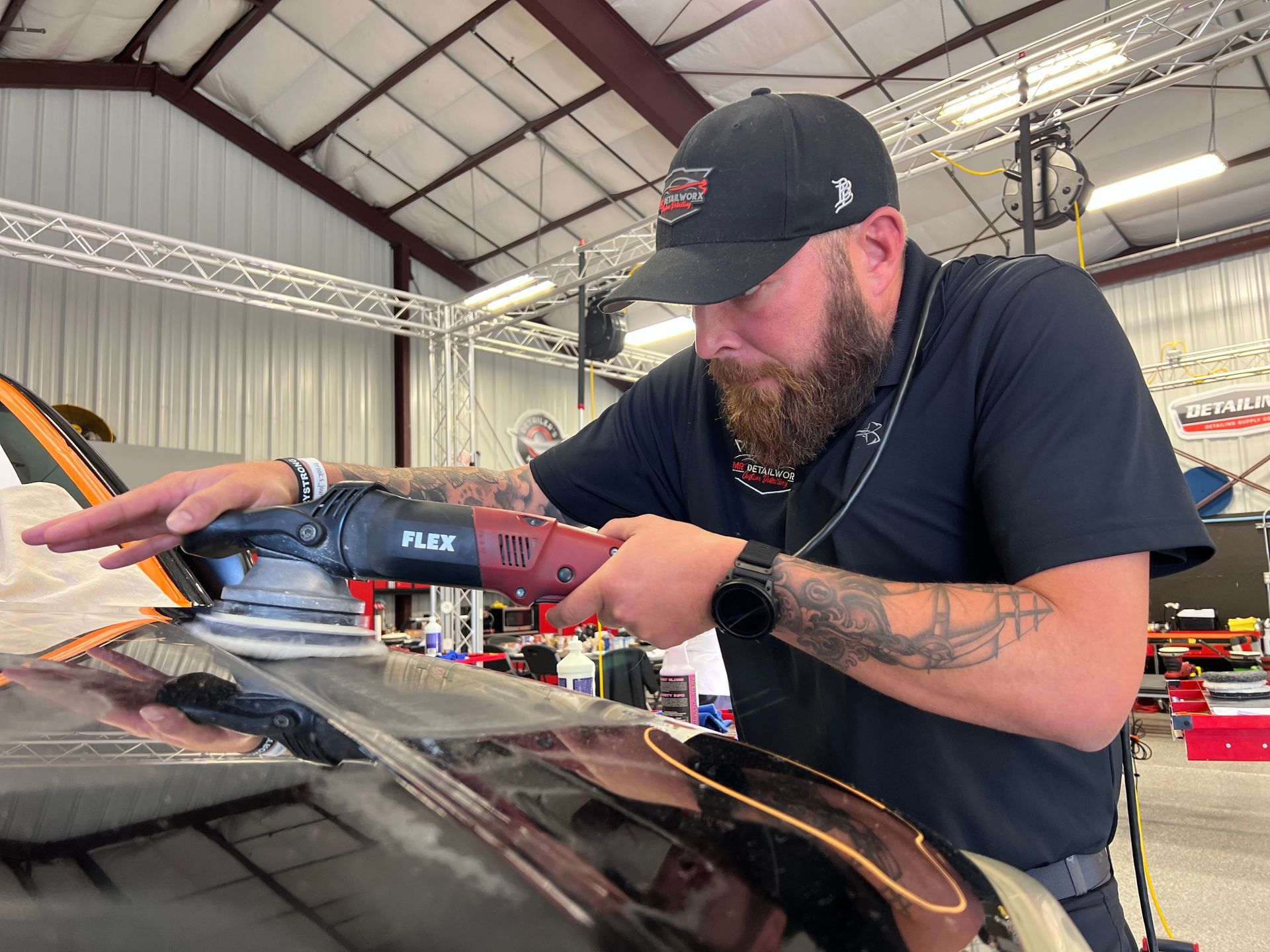 Man in a black cap using a red power sander on a car inside a workshop
