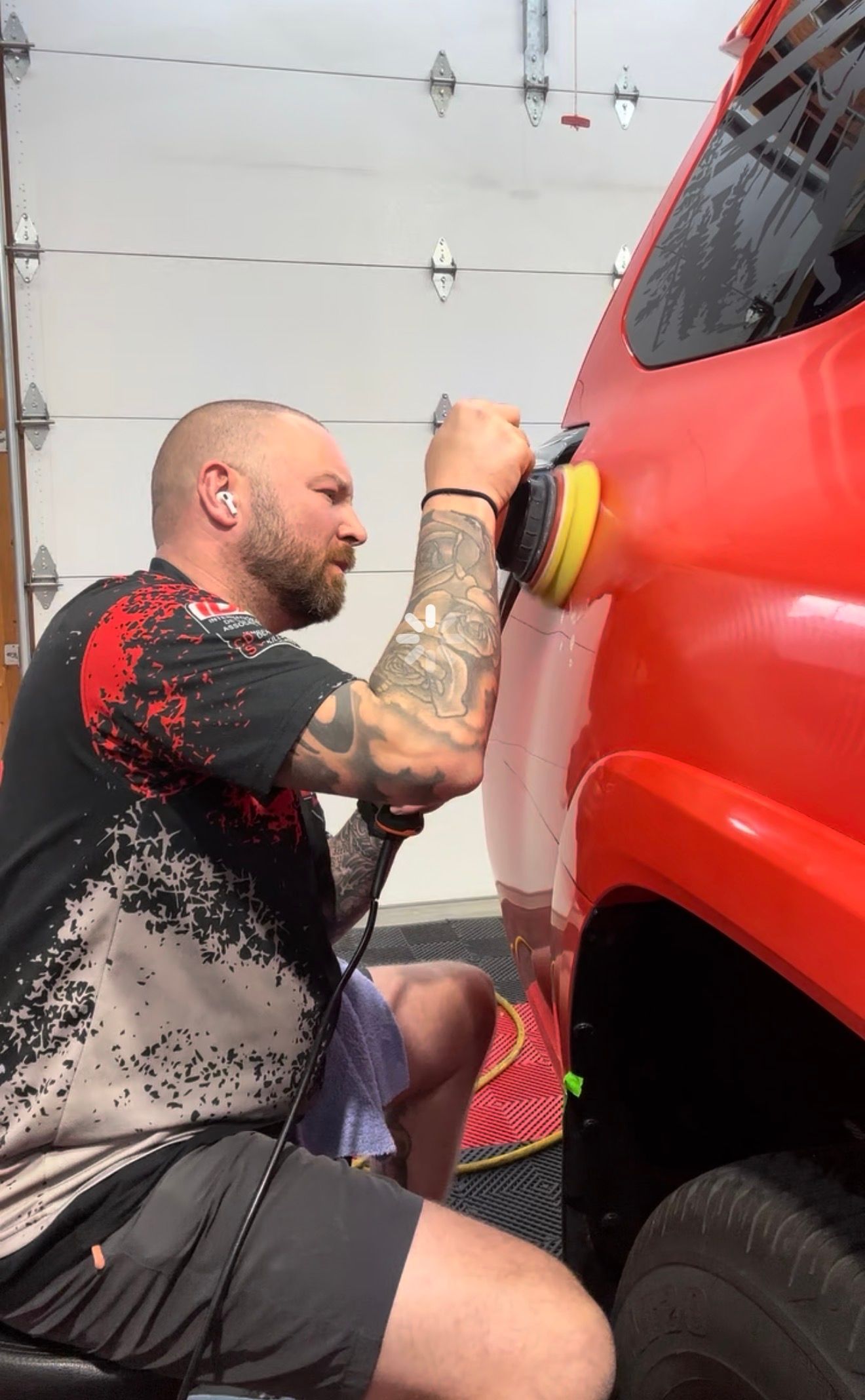 Man polishing a red car door with a buffer in a garage