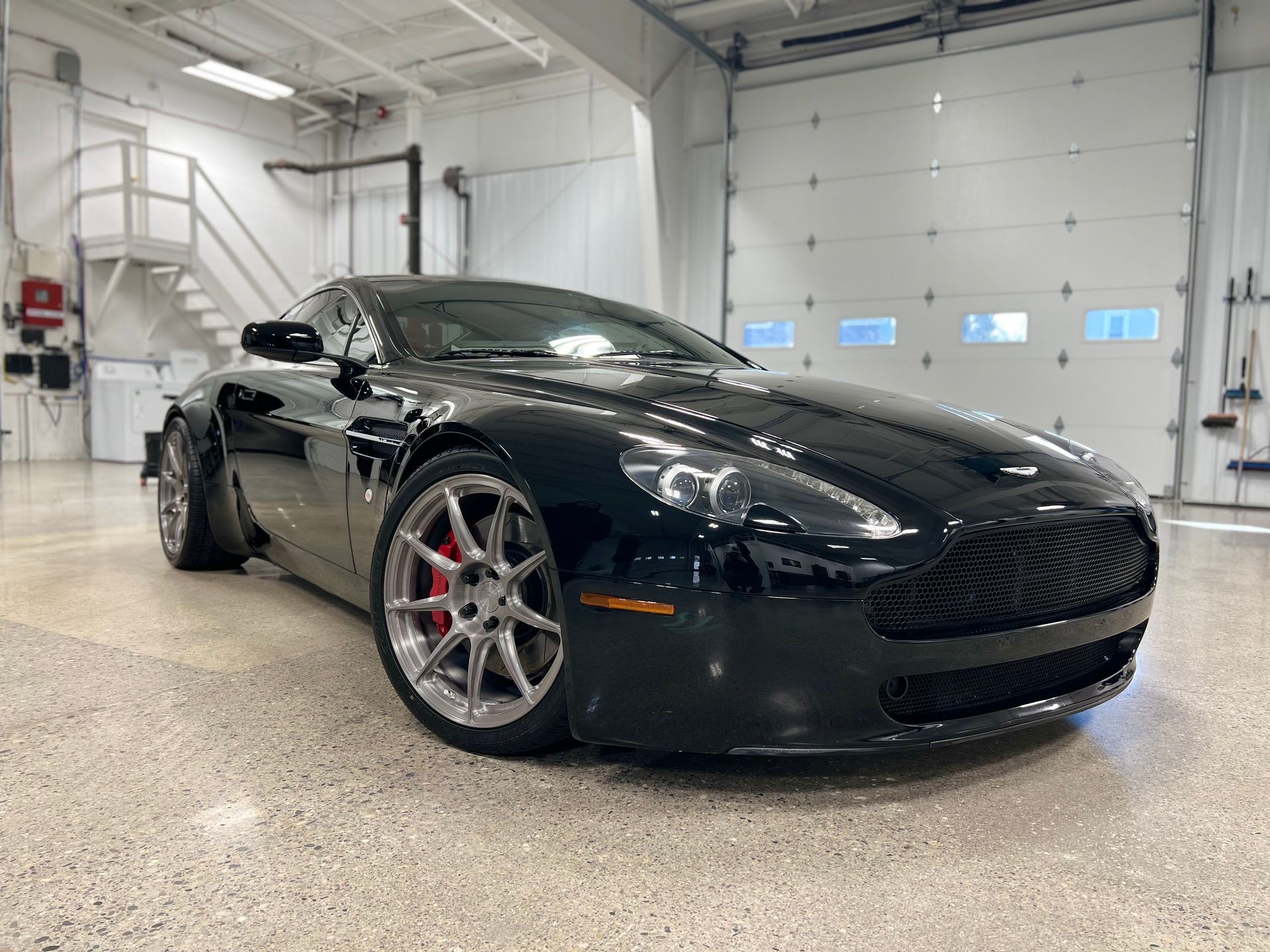 Black sports car parked in a bright industrial garage, viewed from the front-left side.