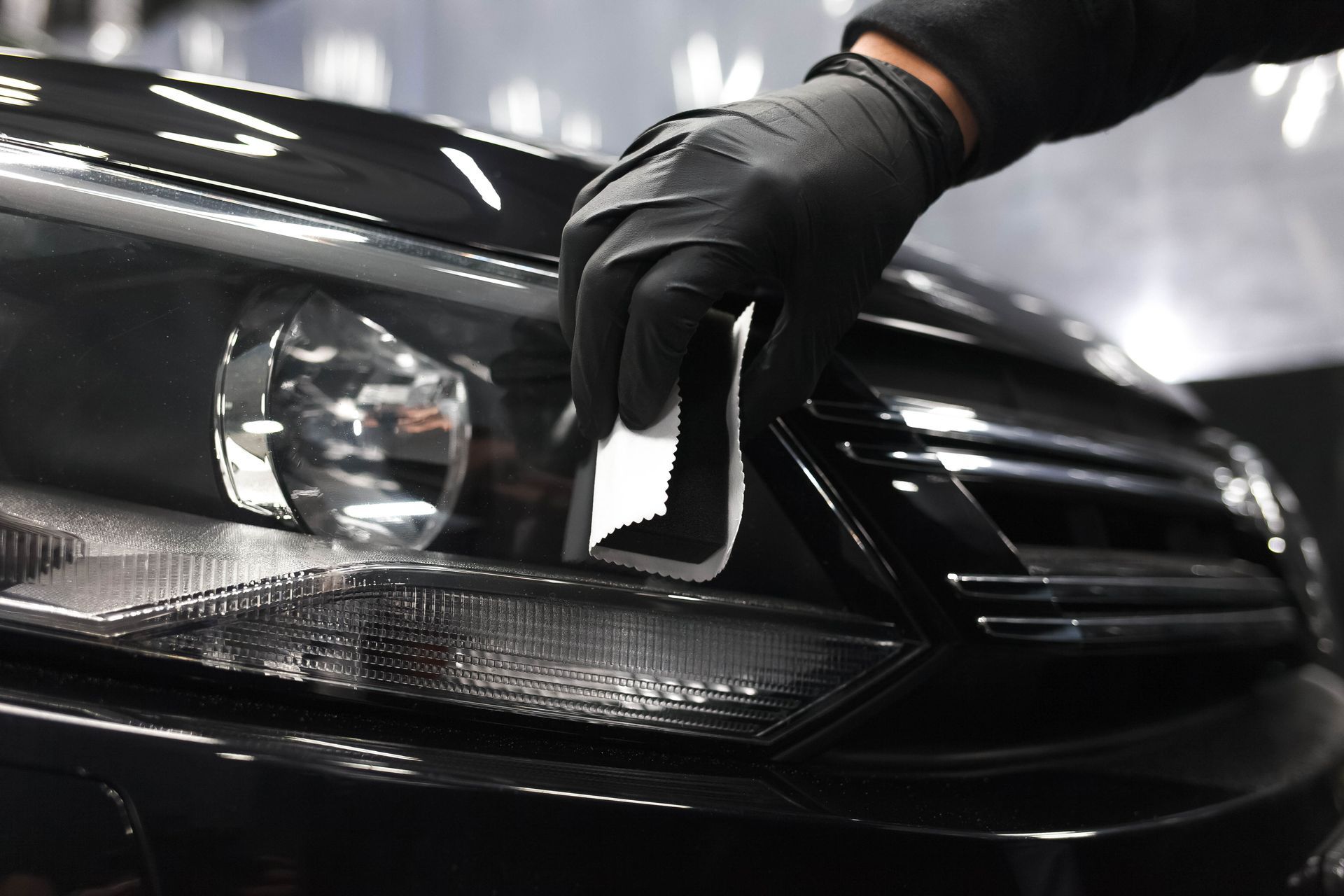 Gloved hand polishing a black car’s headlight with a microfiber cloth
