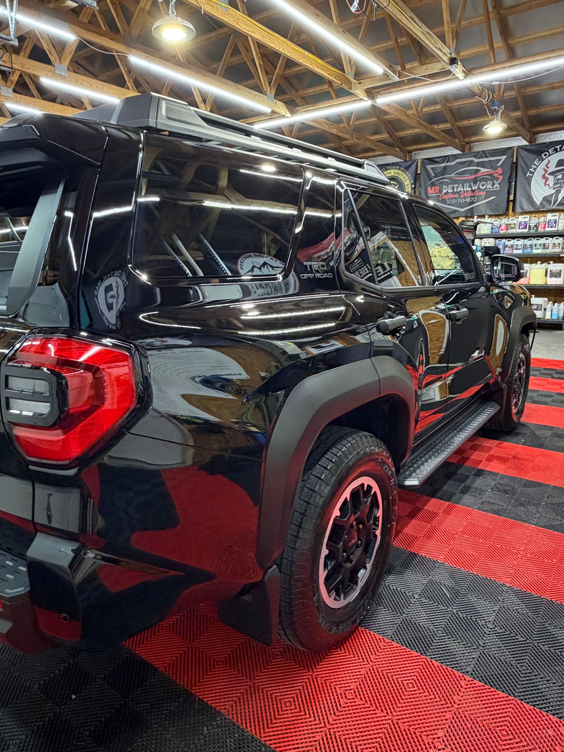 Black SUV with red accents displayed indoors under bright showroom lights, on a red-and-black patterned floor