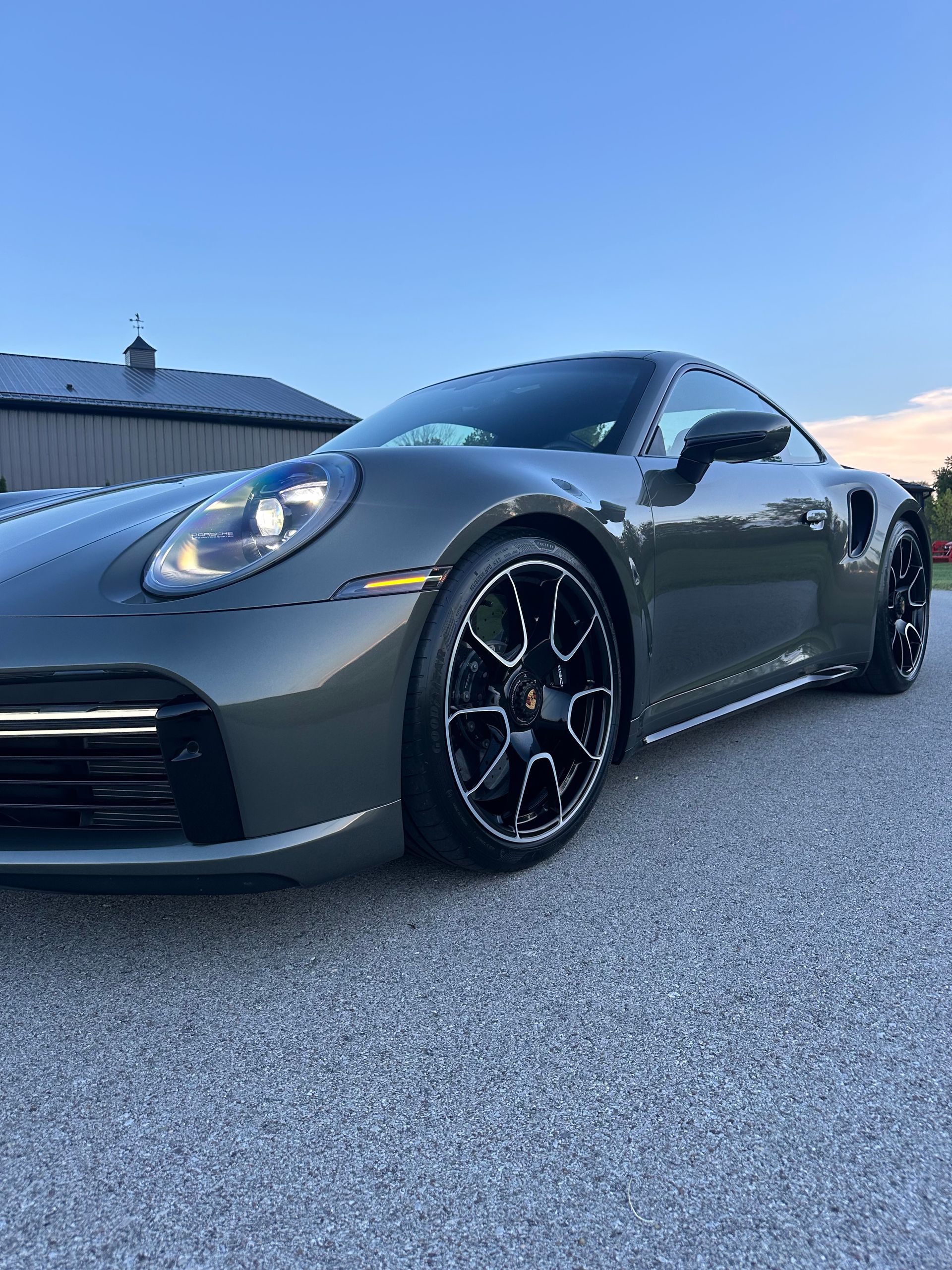 Dark gray sports car parked on a gravel driveway under a blue sky