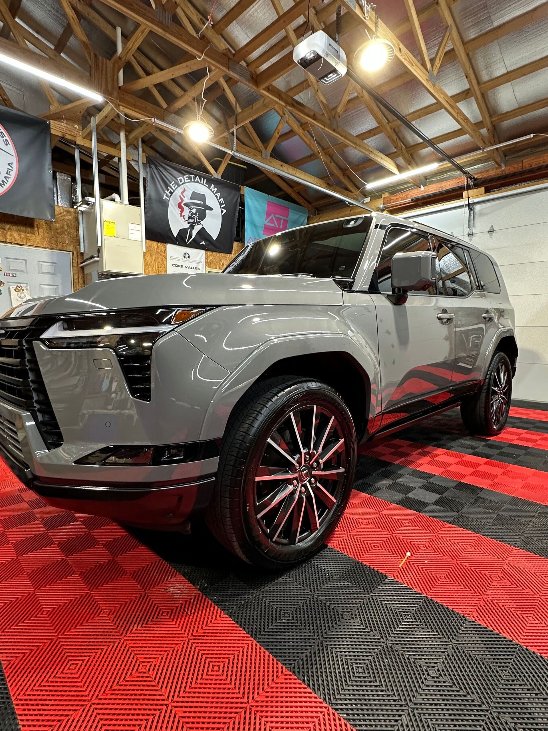 Gray SUV on display in an indoor showroom with red and black patterned flooring and wooden ceiling beams