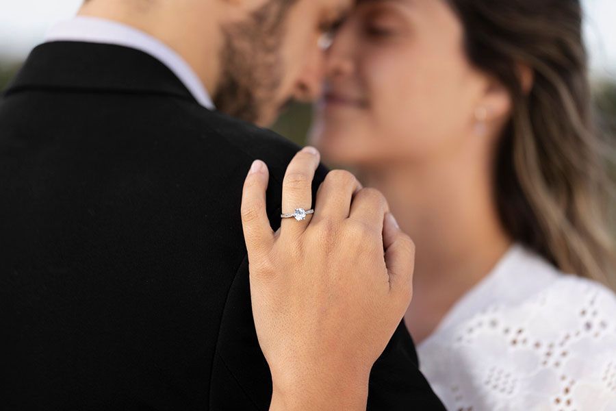 A close-up of a person's hand wearing an engagement ring resting on another person's shoulder.