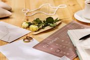 Wedding planning scene with a calendar marked for February 2nd, two gold rings, flowers, and a pearl necklace on a table.