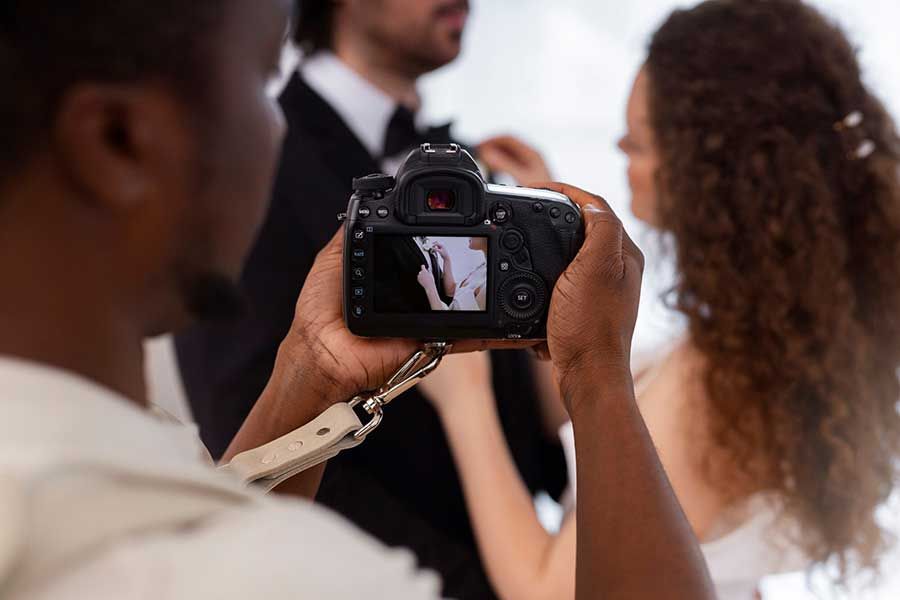 A photographer holds a camera, capturing a close-up shot of a couple in formal wear.