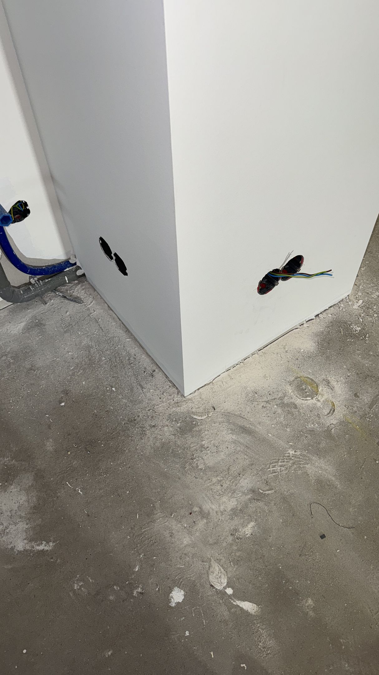 Witte hoekmuur met elektrische draden en gaten op een betonnen vloer.