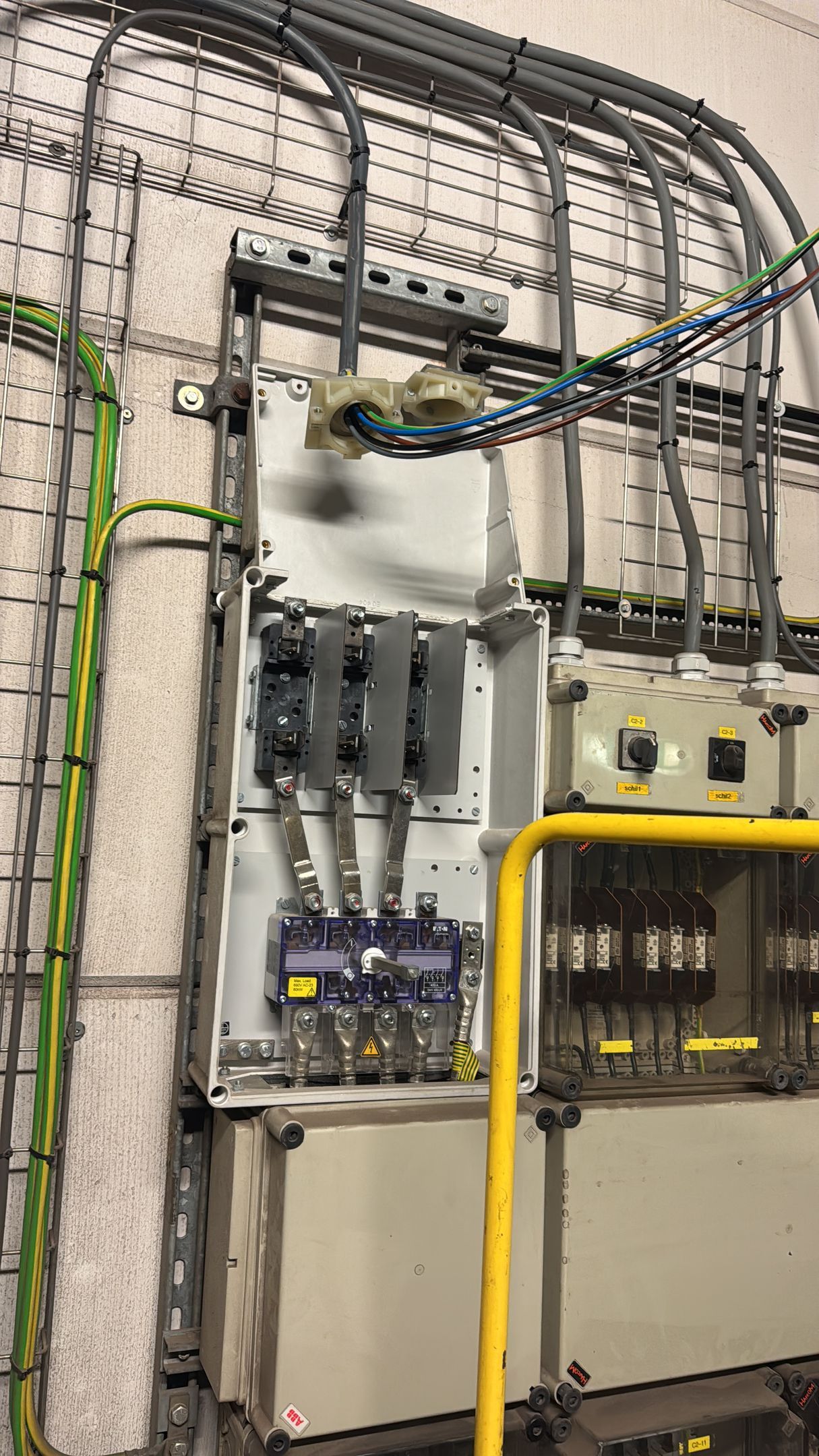 Elektrisch paneel met diverse draden en stroomonderbrekers aan de muur.