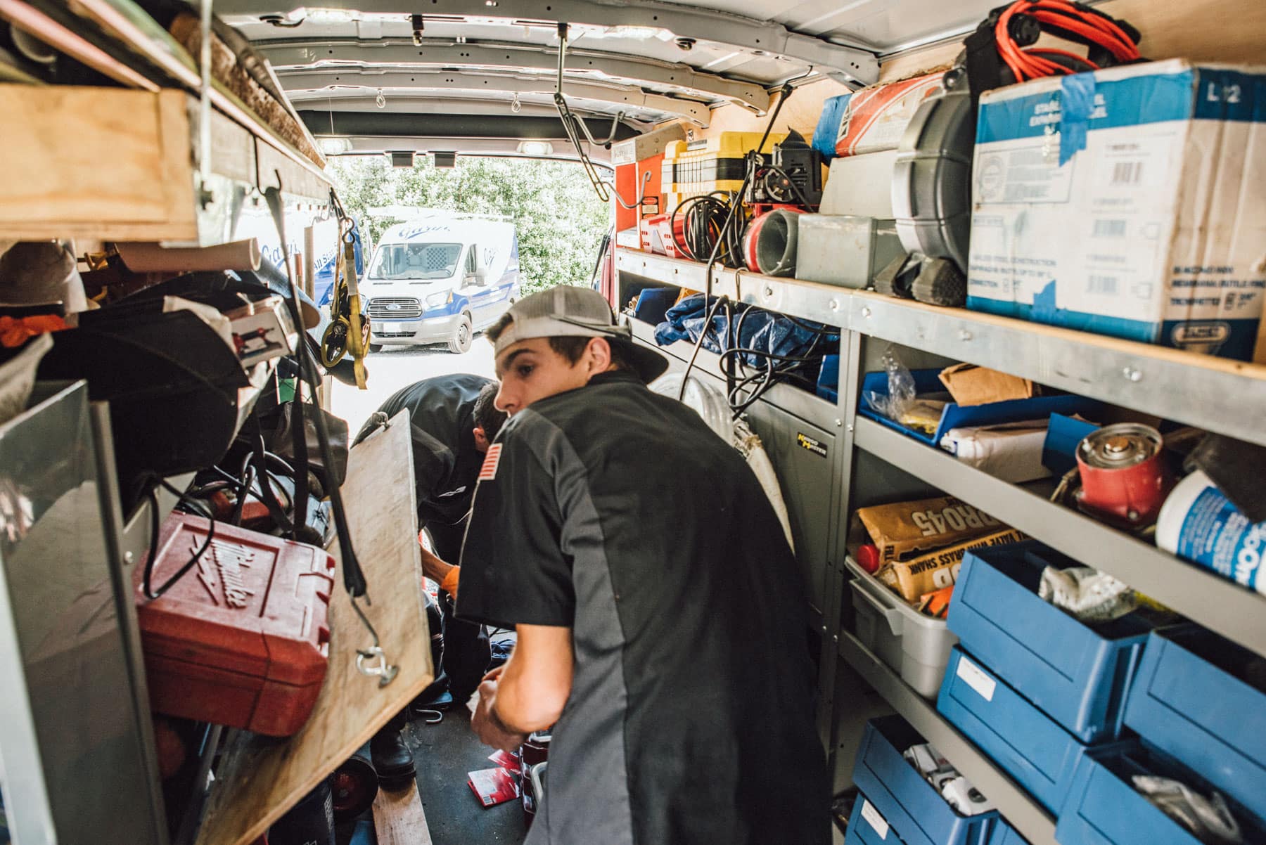 Two men are working in a van filled with tools.