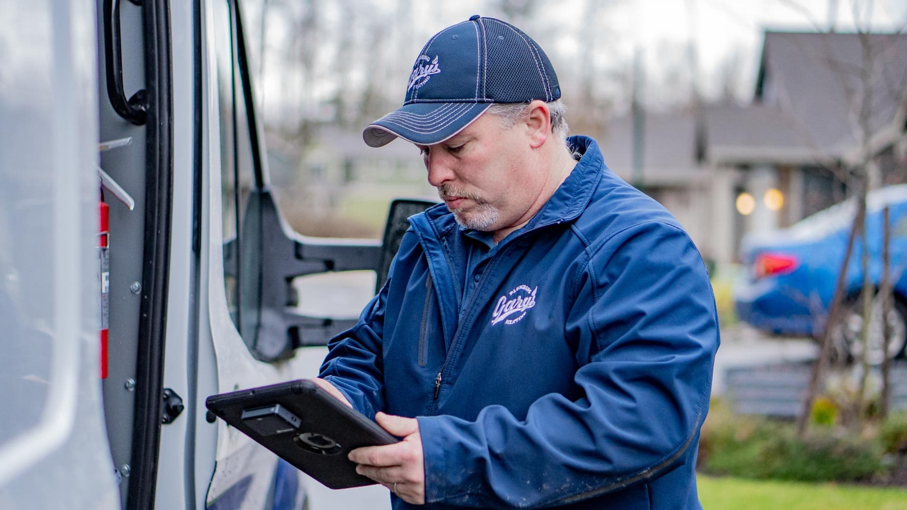 A man is standing next to a van looking at a tablet.