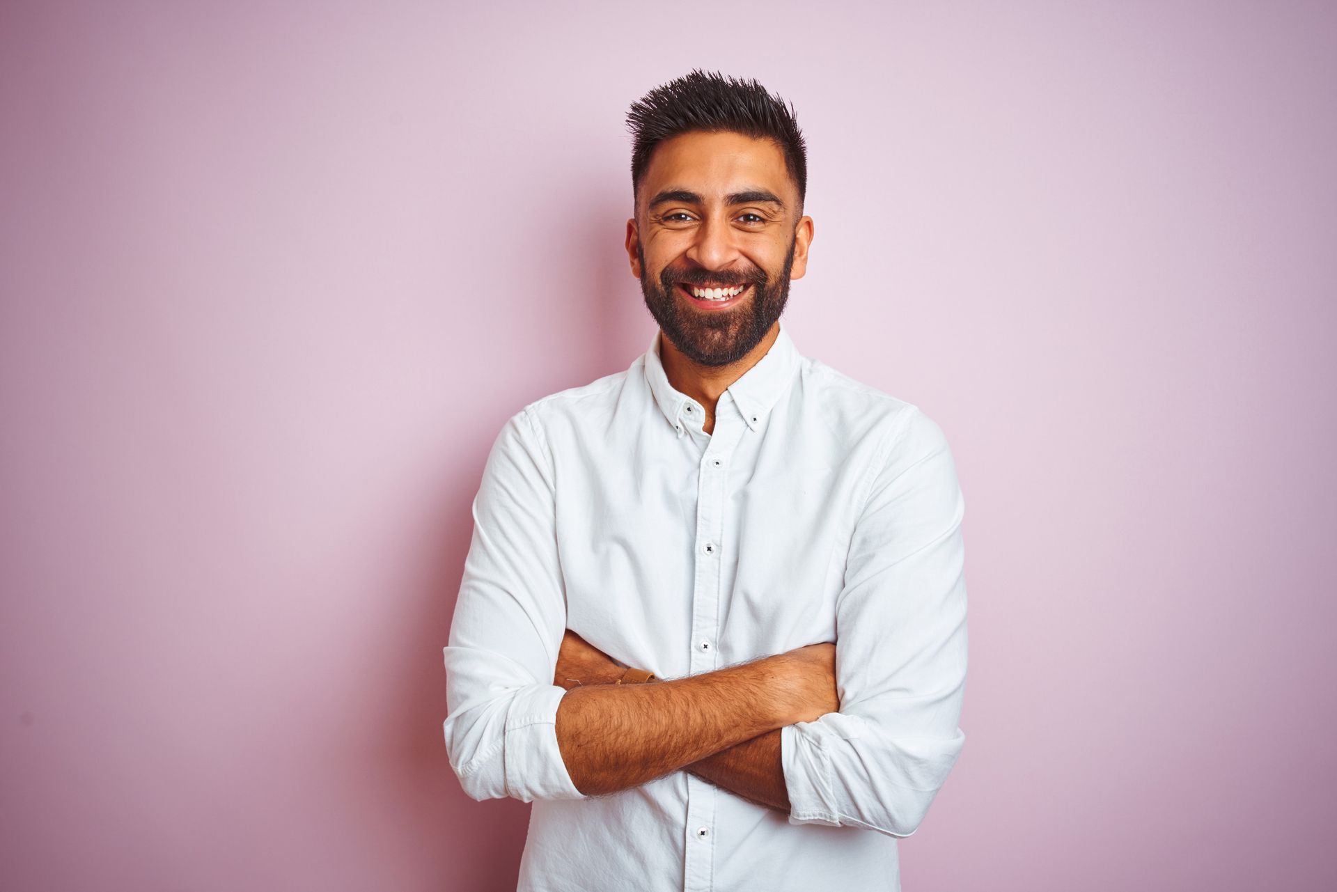 A man with a beard is standing with his arms crossed and smiling.