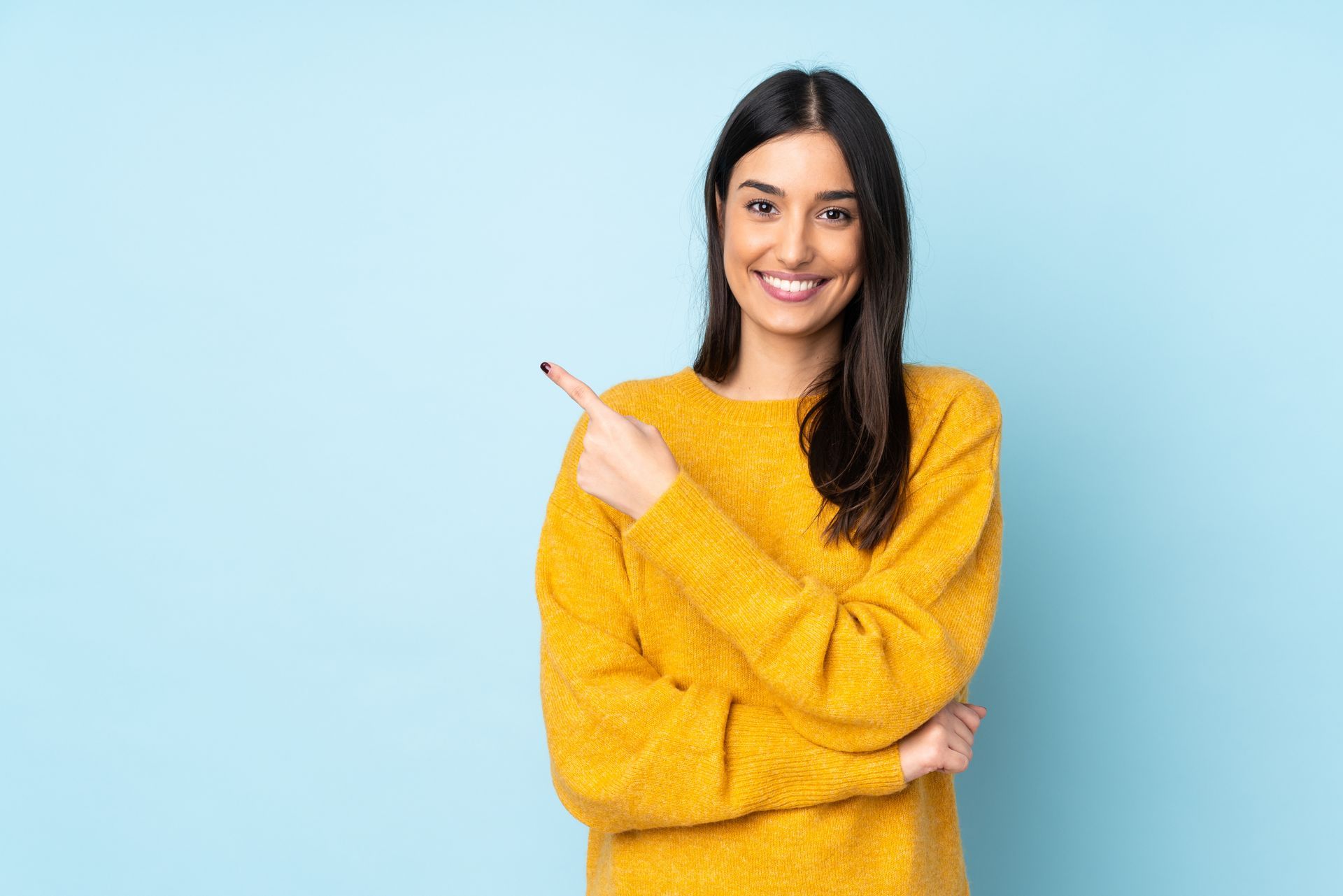 A young woman in a yellow sweater is pointing to the side.