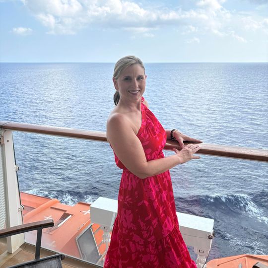 Woman in a red dress smiling on a ship deck with ocean and sky in the background
