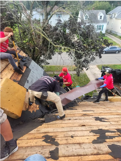Workers on a roof install a large metal panel beside a fallen tree limb.