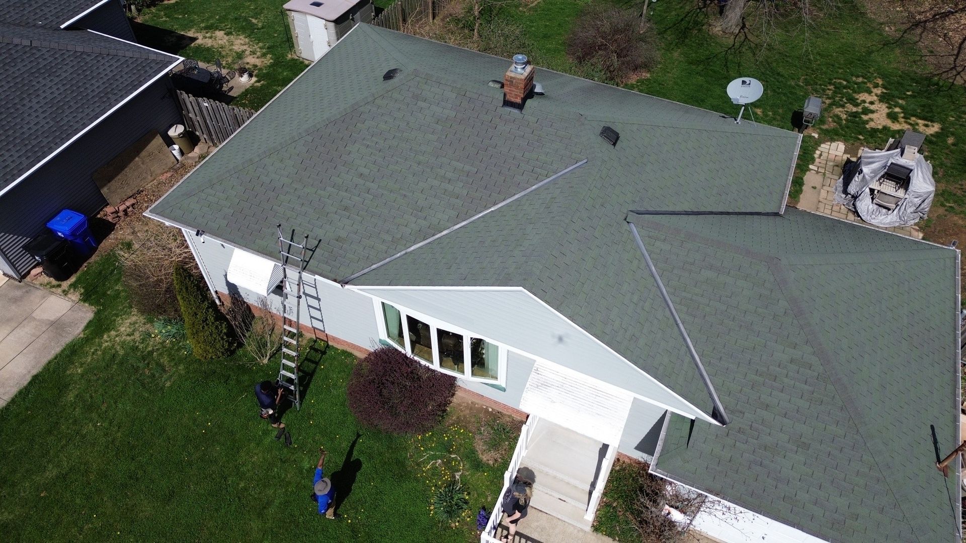 Aerial view of a white house with a green roof and small front yard.