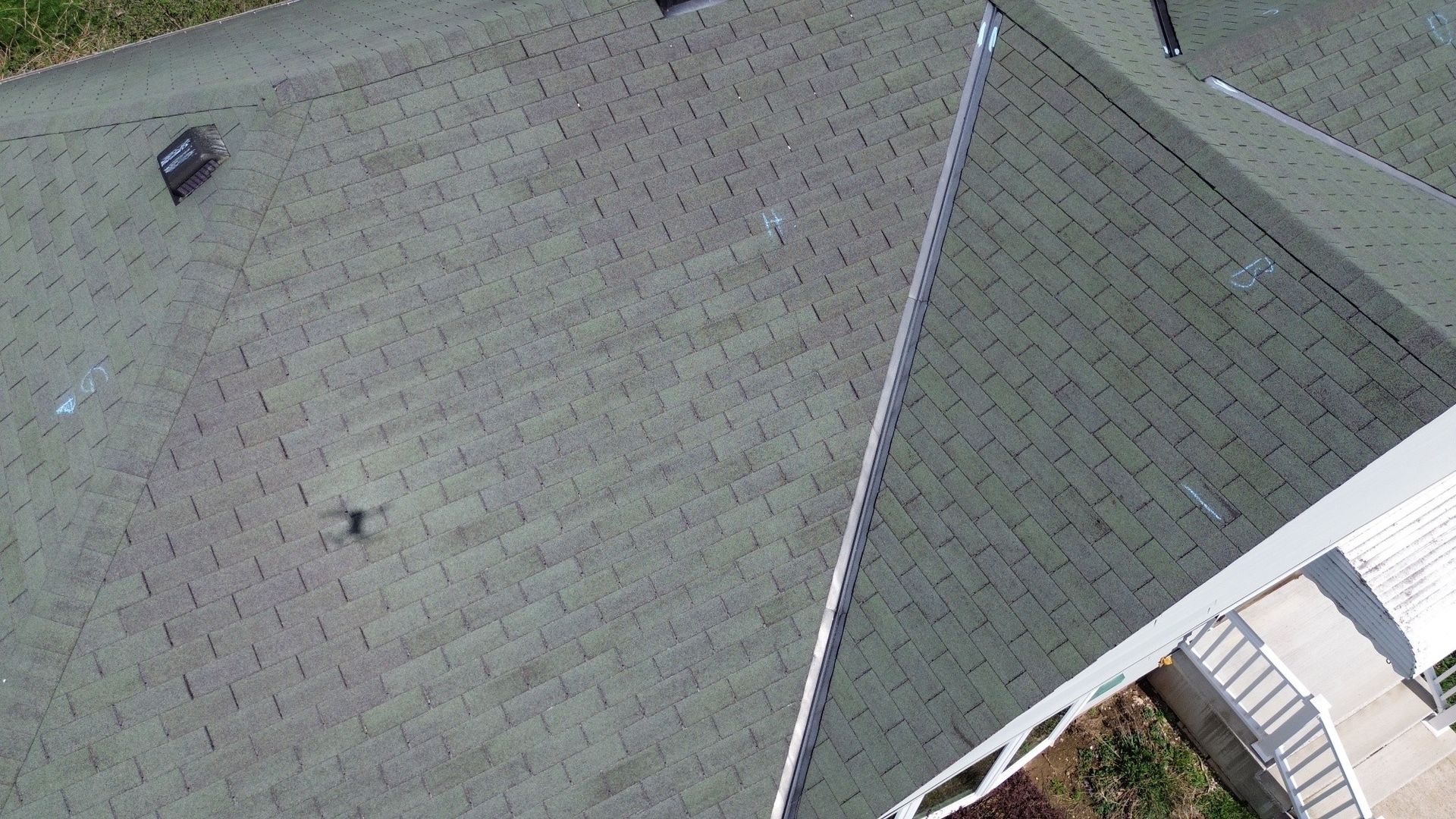 Aerial view of a gray shingled roof with a ridge line and small roof vent near the top left.