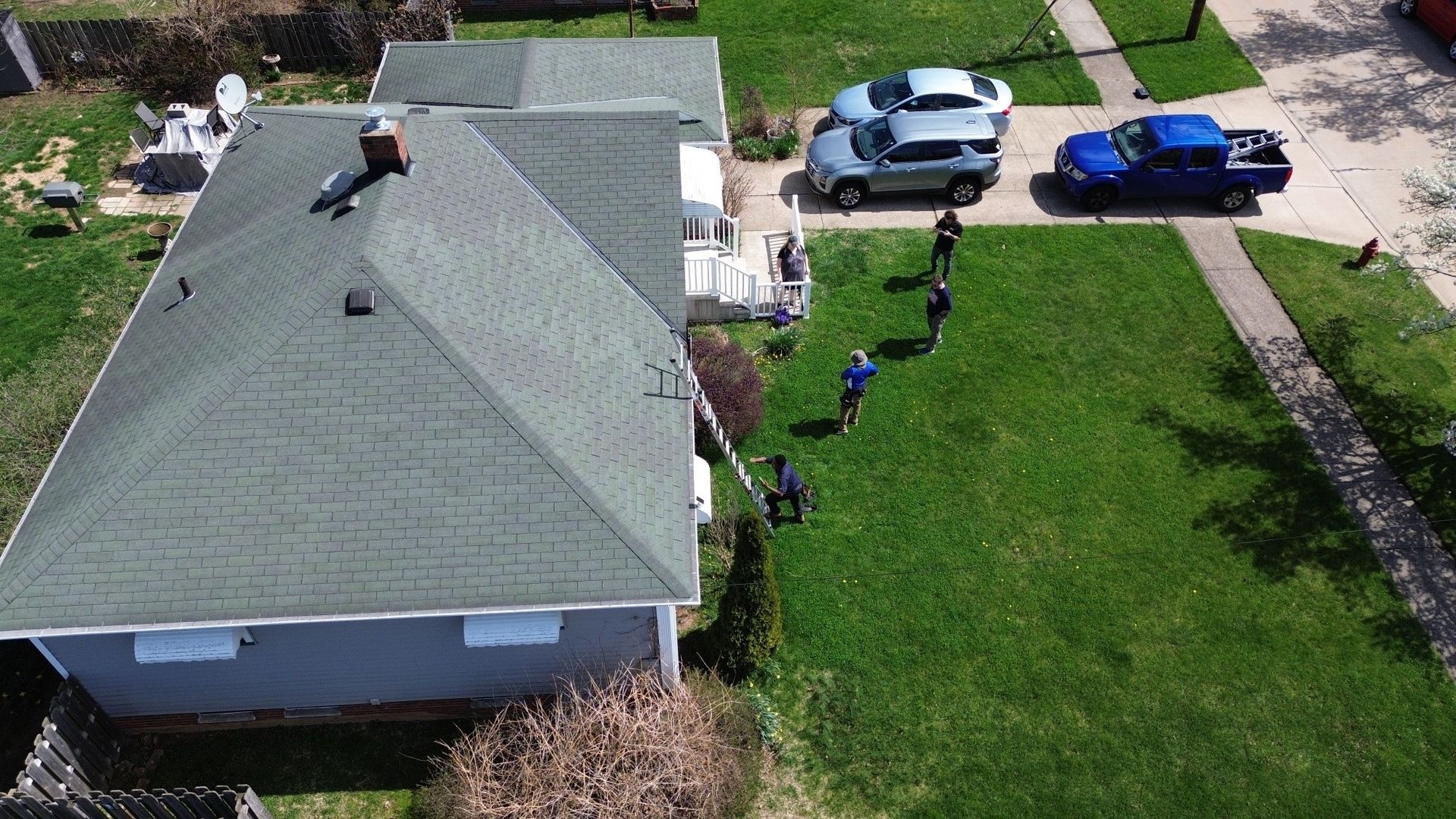 Aerial view of a house, driveway with two cars, and people lined up along the lawn and walkway.
